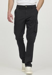 Pantalons cargo noirs avec poches latérales, fabriqués en tissu résistant. Coupe ajustée avec un bouton et une fermeture éclair, associés à des baskets blanches.