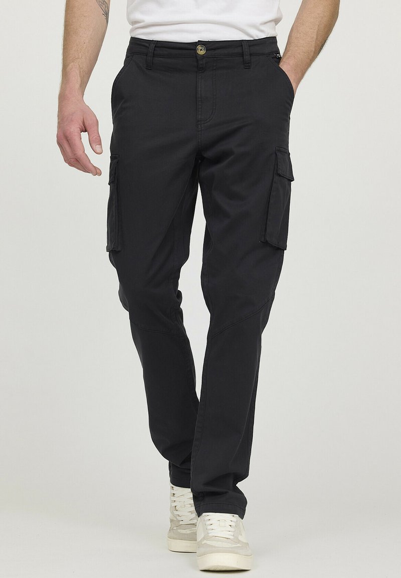 Pantalons cargo noirs avec poches latérales, fabriqués en tissu résistant. Coupe ajustée avec un bouton et une fermeture éclair, associés à des baskets blanches.