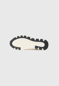 Semelle de sneaker noir et crème avec une surface texturée, à motifs et des rainures pour l'adhérence. Accent de talon noir uni.