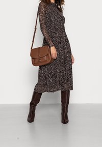 Musta mekko, jossa on läpikuultavat pitkät hihat ja vaaleanbeige eläinkuosilla. Mekko on yhdistetty ruskeaan nahkakorvakotikassiin ja tummiin polvipitkiin saappaisiin.