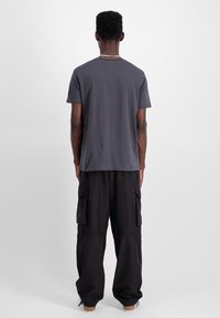 Siva majica s kratkim rukavima, uparena s crnim širokim cargo hlačama s bočnim džepovima. Materijal izgleda mekano i ležerno.