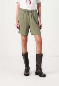 Olijfgroene relaxte shorts met een elastische tailleband en een trekkoord. Bruine kniehoge laarzen met gespsaccents.