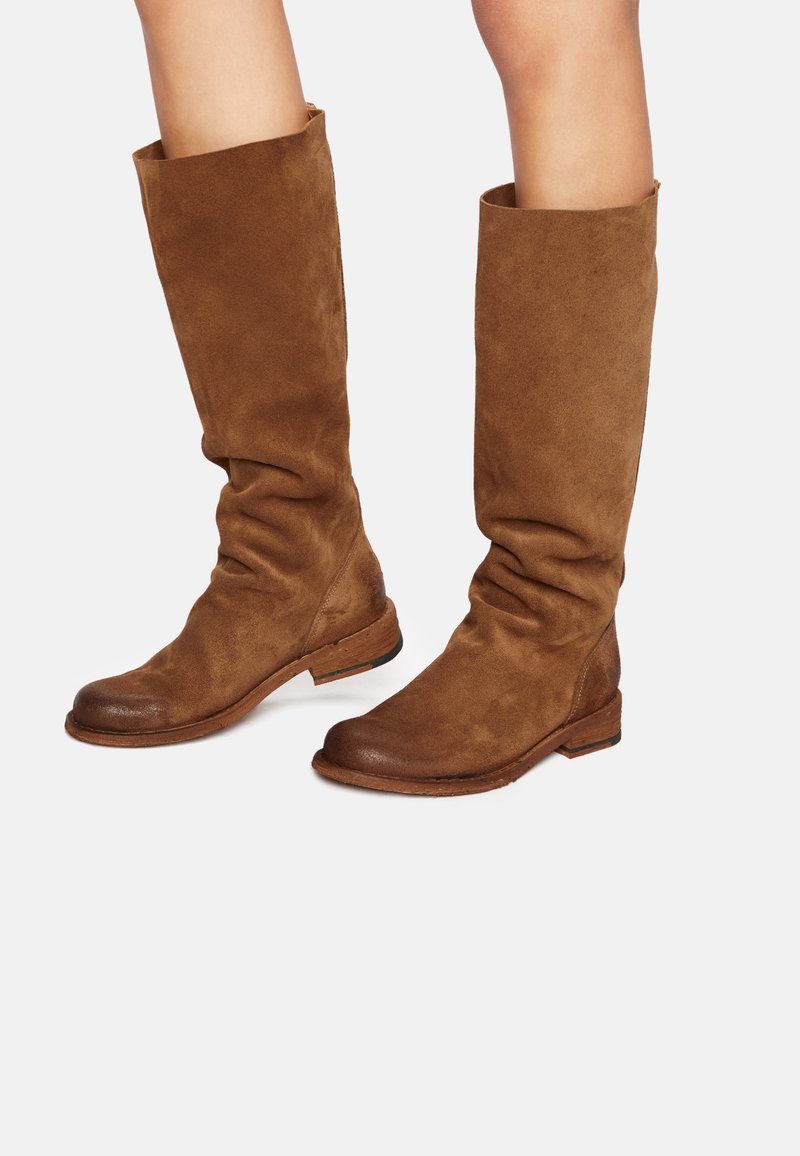 Bottes en suède marron jusqu'au genou avec un design décontracté, semelle plate et bout arrondi. Le matériau a une texture douce et un léger éclat.