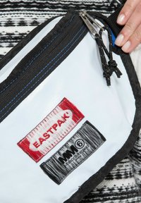 Borsa bianca con bordi neri, caratterizzata da etichette ricamate in rosso e nero. Doppie zip, tessuto testurizzato e design leggero.