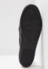 Semelle de chaussure noire avec une surface texturée, arborant un logo "MK" audacieux et le nom "Michael Kors" en relief. Design en caoutchouc durable.