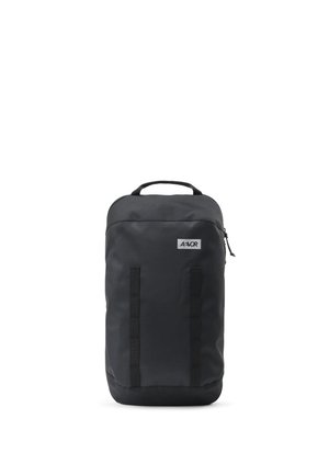 Schwarzer rechteckiger Rucksack mit einem oberen Griff, vorderen vertikalen Riemen und einem kleinen Logo-Patch nahe der oberen rechten Ecke.