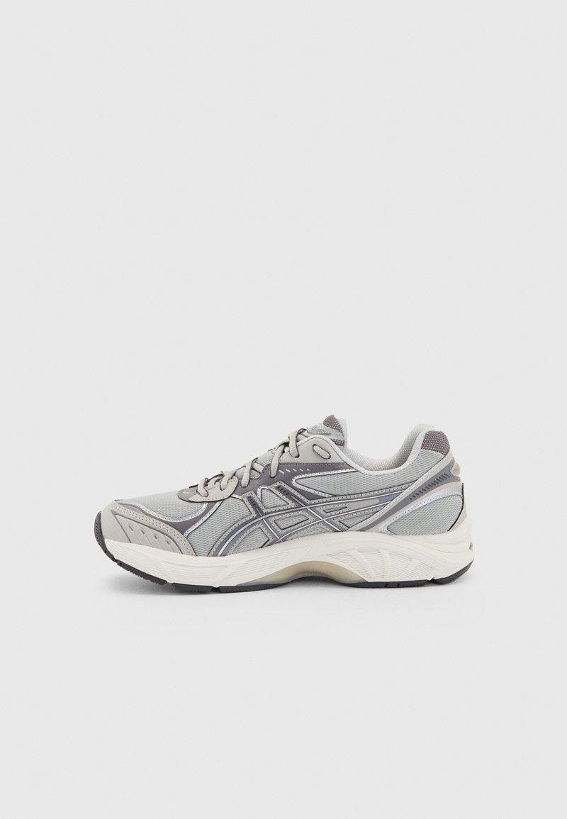 Baskets de sport gris et blanc avec superpositions en mesh et synthétique, fermeture à lacets et semelle rembourrée, présentées en vue latérale sur un fond uni.