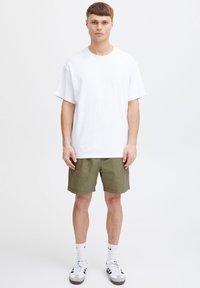 Valge lühikeste varrukatega T-särk, lahtise lõikega, sobitatud oliivroheliste pükstega. Modell kannab valgeid sokke ja must-valgeid tossusid. Lihtne disain.