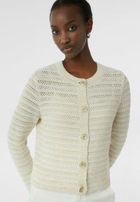 Gebreide cardigan in crèmekleur met een gestreept patroon, ronde hals en vijf knoopsluitingen, met een zachte textuur en subtiele glans.