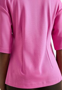 Rosa kortärmad topp med en strukturerad yta, som har sidofållar och en rak fåll. Tyget ser slätt och lätt ut.