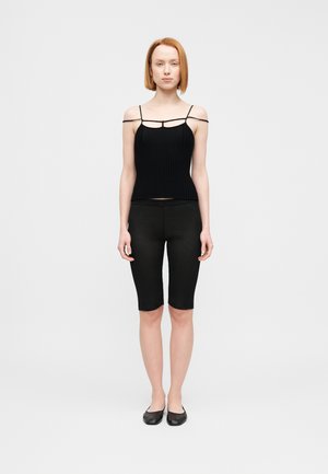 Czarny prążkowany top na ramiączkach, zestawiony z czarnymi legginsami do kolan. Noszony z prostymi czarnymi płaskimi butami. Gładkie tło.