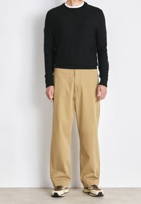 Maglione nero a maglia con collo rotondo, pantaloni beige a gamba larga e sneakers multicolori. Design semplice, senza motivi o decorazioni visibili.