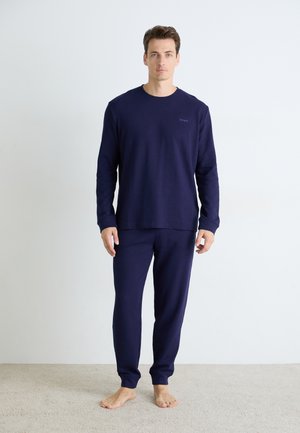Navy lounge-set med langermet topp og bukser. Vaffeltekstur, ribbede mansjetter og kant. Liten logo på brystet. Myk, avslappet passform.