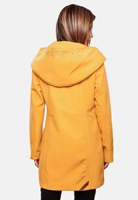Abrigo amarillo con capucha de textura suave. Presenta un logotipo bordado en la capucha y un corte entallado, con acentos laterales cerca del dobladillo.