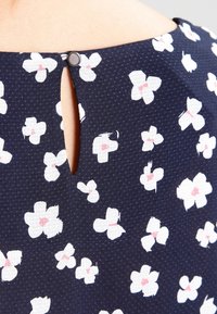 Navy fabric blouse with white floral pattern and pink accents. Features a keyhole opening at the back secured with a small button.