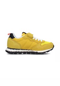 Sneaker gialla in suede con lacci bianchi, suola a zig zag bianca e nera, collare imbottito e un'etichetta rossa sul retro. Pannello frontale ventilato.