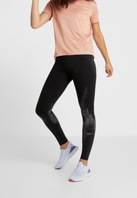 Svarta leggings med en gradient av vita prickar och en lila Nike-logotyp, kombinerat med en ljusrosa kortärmad tröja och vita träningsskor.