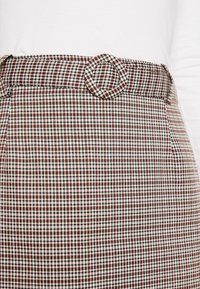 Gonna a scacchi in rosso, nero e bianco con un tessuto testurizzato. Presenta una fibbia rotonda in vita e due tasche laterali.