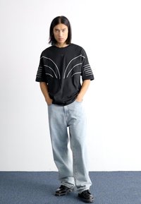 Black oversized short-sleeve shirt with white line patterns, paired with light blue loose-fitting jeans and black shoes. Simple, casual design.