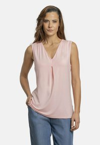 Blusa sin mangas de color rosa con escote en V y un pliegue central; tejido suave con una textura lisa; combinada con pantalones azules holgados.