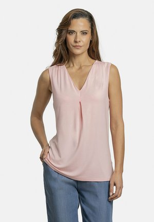 Blusa sin mangas de color rosa con escote en V y un pliegue central; tejido suave con una textura lisa; combinada con pantalones azules holgados.