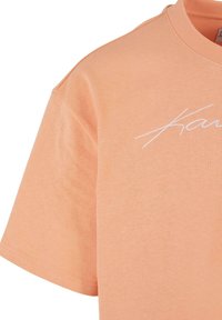 Ferskenfarget bomull t-skjorte med korte ermer. Har en hvit brodert skript-logo på brystet og en ribbestrikket halsringning.