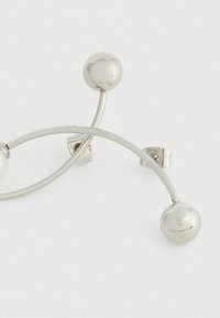 Anello in metallo argentato con design curvo, caratterizzato da tre accenti sferici. Texture liscia e estetica minimalista, con dettagli di chiusura ben definiti.