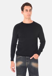 Maglione nero lavorato a maglia con scollatura tonda e polsini a costine, abbinato a jeans blu sbiaditi. Il tessuto sembra morbido e strutturato.