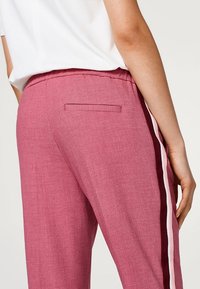 Roze, gestructureerde broek met een achterzak, voorzien van horizontale witte en bordeauxrode strepen langs de zijkanten. Inclusief elastische tailleband.