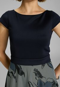 Top azul marino con mangas cortas y escote redondeado, combinado con una falda plizada que presenta patrones florales en negro y rayas verticales.