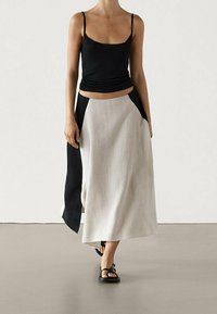 Zwart aansluitend topje gecombineerd met een vloeiende, hooggeregde rok met een zwart zijpaneel en lichtgrijs stof. Gladde textuur en enkel lengte.