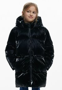 Sort, blank pufferjakke med hætte, med lynlåslukning og snøre i taljen. Rundede skuldre og sidelommer.