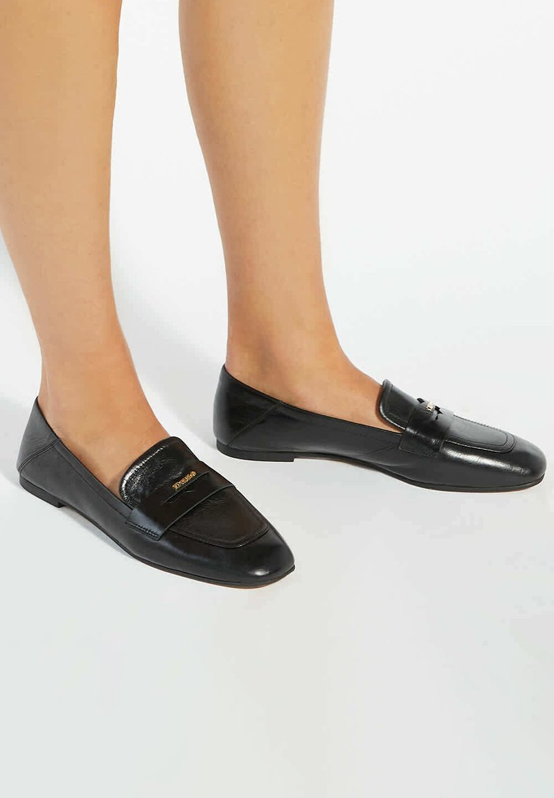 Zwarte loafers met een mix van matte en glanzende lederen texturen, puntige neus en een accentstrap met gouden logo-detail. Plat profiel.