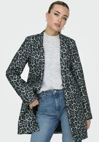Manteau long en imprimé léopard gris et noir, fabriqué en tissu doux, avec un col cranté, une ouverture sur le devant et des manches longues. Porté par-dessus un pull gris.