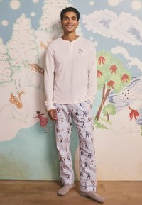Camisa henley de manga larga de color claro con un pequeño gráfico. Pantalones de pijama estampados con figuras practicando deportes de invierno. Textura suave.