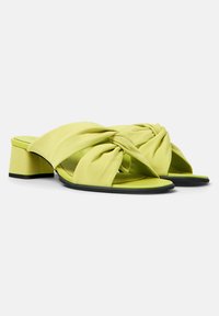 Mule verde lime con parte superiore in morbido tessuto annodato, design open toe e tacco blocco. Contrasto nero sulla suola per un tocco di dettaglio.