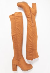Brune over-the-knee støvler lavet af blødt nubuck-lignende materiale, med en robust blokhæl, lynlås på siden og struktureret sål for godt greb.