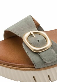 Sandale en daim vert avec une semelle intérieure en cuir marron, dotée d'une grosse boucle dorée et d'une semelle épaisse en caoutchouc blanc. Accents texturés sur toute la surface.