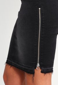 Svart denim minikjol med synlig silverfärgad dragkedja på sidan, fransad nederkant och figursydd design. Texturerad, slitstark tyg utan utsmyckningar.