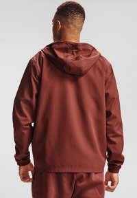 Chaqueta de sudadera color burdeos con capucha, puños elásticos y una textura suave. La parte trasera presenta un diseño simple sin logotipos ni patrones.