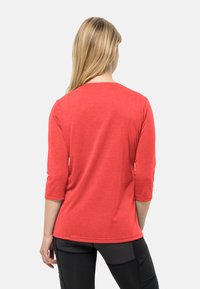 Maglietta rossa a maniche tre quarti realizzata in un tessuto morbido, con collo rotondo e un design aderente, abbinata a leggings neri.