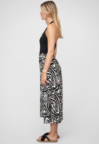 Haut halter noir associé à une jupe maxi à imprimé zèbre noir et blanc. La jupe présente un design fluide, atteignant le mi-mollet, avec une texture lisse.