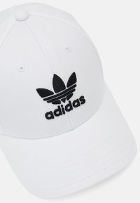 Gorra blanca hecha de tela suave, con un logotipo de Adidas bordado en negro que presenta las tres bandas y un diseño clásico de seis paneles.
