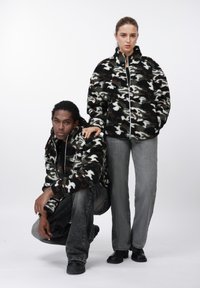 Fleece jakker med lynlås i sort, hvid og brun camouflagemønster. Model iført grå jeans og sorte støvler; en anden model i lignende jakke.