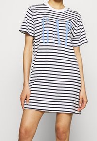 Sukienka t-shirt w paski w kolorze białym i granatowym, z dużym jasnoniebieskim logo "GAP", krótkimi rękawami i okrągłym dekoltem. Miękka tkanina.