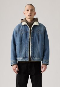 Denim jacket in light blue with a Sherpa-lined collar and dark brown inner hoodie, featuring a relaxed fit and front button closure.