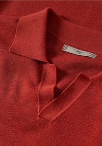 Polo en maille rouge avec un col plié et un décolleté en V ouvert laissant visible une étiquette de la marque MNG à l'intérieur du col.