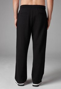 Black sweatpants with an elastic waistband, two back pockets, and a relaxed fit, made from soft fabric, paired with white shoes.