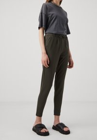 Kurzärmliges, dunkelgraues T-Shirt mit lockerer Passform, kombiniert mit olivgrünen, schmal zulaufenden Hosen und schwarzen Rutschen-Sandalen.