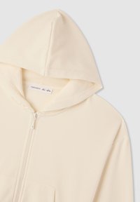 Felpa con zip color crema realizzata in tessuto morbido, con cappuccio, zip centrale e tasca frontale. Design semplice e funzionale.
